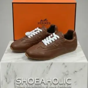 حذاء رياضي من الجلد البني الفاخر مع صندوق العلامة التجارية، يعكس الأناقة والجودة العالية في البحرين. ||| Premium brown leather sneakers displayed with a signature luxury brand box on a minimalist background.